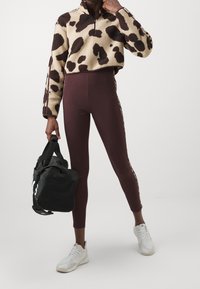 Brun och beige fleece-tröja med dragkedja, koskinnsmönster; vinröda höga leggings; svart träningsväska; vita sneakers.