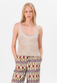 Top senza maniche di un leggero beige con scollatura rotonda e tessuto testurizzato, caratterizzato da una scritta stampata sottile. Abbinato a pantaloni multicolori con motivo.