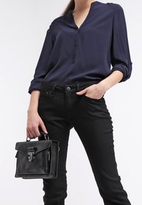 Blusa de marina con escote en V y tres botones, combinada con jeans negros ajustados. La modelo sostiene un pequeño bolso de piel negra con cierre.