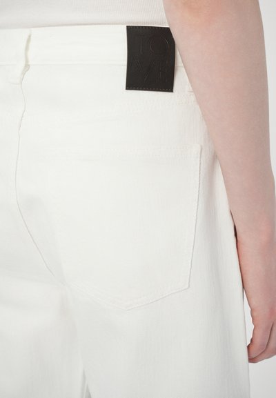 Pantalon en denim blanc mettant en avant un gros plan sur la poche arrière et une étiquette en cuir noir avec "TOVE" embossé. Tissu résistant, coupe droite.