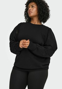 Črna trenirka s puf rokavi, okrašena z rastlinskimi vzorci z izrezi. Iz mehke tkanine, z rebrastimi manšetami in spodnjim robom.