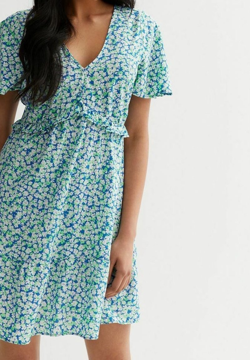 Kukkakuvioinen mekko, jossa on V-aukko, lyhyet hihat ja kevyt, liehuva helma. Mekossa on sinisen, vihreän ja valkoisen sävyinen kukkakuosi vaalealla pohjalla.