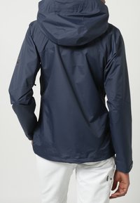 Granatowa wodoodporna kurtka z kapturem, gładką fakturą, elastycznymi mankietami oraz naszywką z logo na lewym rękawie. Widok od tyłu.