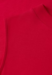 Haut sans manches rouge vif avec un col rond, présenté plié sur un fond en tissu rouge assorti.