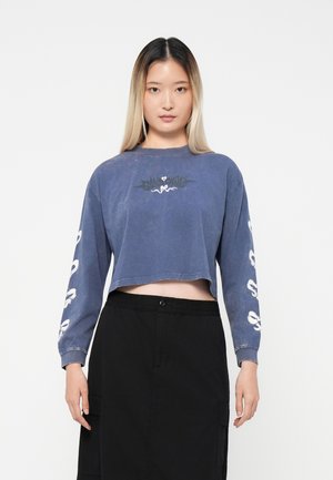 Camicia a maniche lunghe tagliata in cotone blu sbiadito, con un design grafico nero sul petto e stampe bianche su entrambe le maniche.