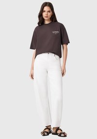 Σκούρο γκρι φαρδιά μπλούζα με λογότυπο, συνδυασμένη με λευκό παντελόνι φαρδιάς γραμμής και παπούτσια slip-on με σχέδια. Απλός σχεδιασμός, καθημερινή εμφάνιση.