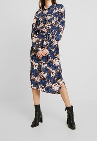 Blommig skjortklänning med långa ärmar, marinblå bakgrund, krämfärgad och brun blommönster, midjebälte, sidov slit, matchad med svarta ankelstövlar.