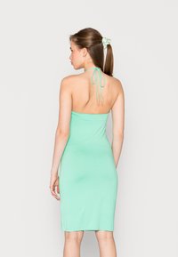 Um vestido bodycon sem mangas, em verde menta, com decote halter e fecho de laço nas costas. Textura suave, design até aos joelhos.