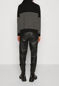 Maglione nero a maglia con strisce orizzontali bianche, abbinato a pantaloni in pelle neri a vita alta e stivali neri alla caviglia robusti.