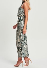 Vestido maxi con un patrón de remolinos en verde y beige, con cuello halter, que presenta una silueta fluida y se combina con sandalias nude de tiras.