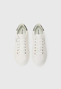 White leather sneakers with black heel accents, metal eyelets, and flat laces. Features brand logo on the side and padded collar for comfort.
