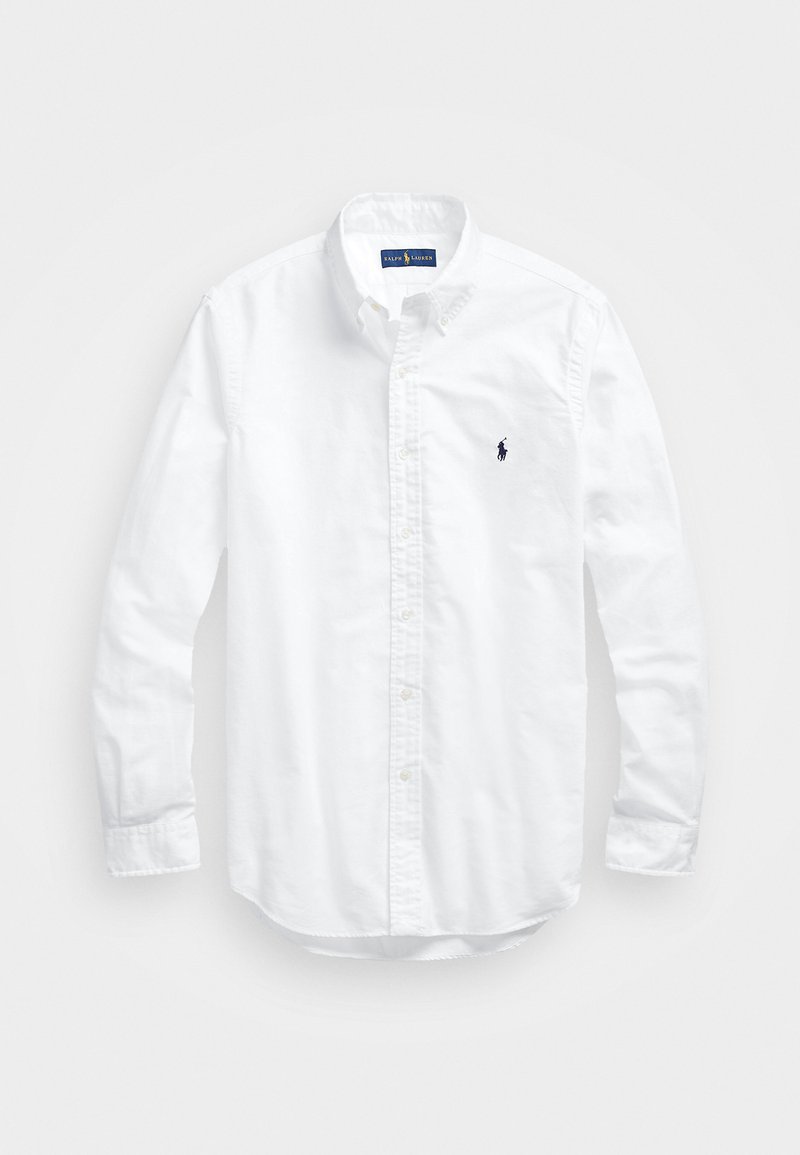 Valkoinen pitkähihaisessa napitetussa paidassa, joka on valmistettu puuvillasta. Siinä on klassinen kaulus, napilliset hihansuut ja pieni tummansininen brodeerattu logo rinnassa.