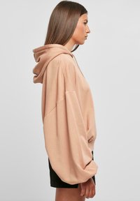 Üks suur peach värvi kapuutsiga pusa, millel on laiad varrukad ja pehme tekstuur. Kombineeritud mustade pükstega, minimalistlik disain.