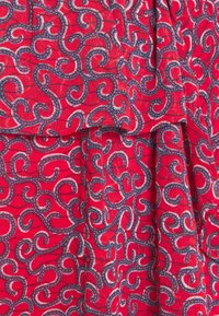 Röd tyg med ett virvlande mönster i marinblått och vitt, med en texturerad yta. Materialet hänger mjukt och visar detaljer av designen.