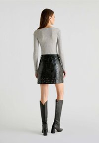 Falda de cuero negra con detalles de ojal en el dobladillo, combinada con una blusa de manga larga ajustada gris y botas negras de tacón alto hasta la rodilla.
