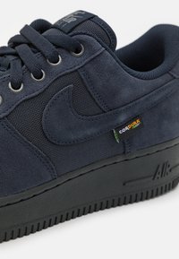 Adidași bleumarin din material suede și plasă, cu talpă neagră, închidere cu șireturi, logo Nike Swoosh și o etichetă mică din material Cordura pe lateral.