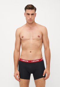 Črne moške bokserice z rdečim logotipom Levi's na pasu. Tkanina je videti gladka in raztegljiva ter se prilega tesno.
