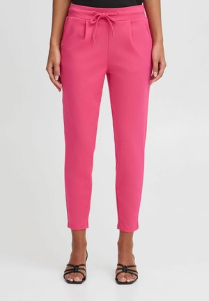 Rozā vieglie bikses ar aukliņu jostas, sašaurinātiem galiem un sānu kabatām, apvienoti ar melniem sandaliem uz siksniņām.