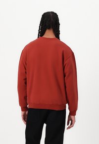 Rød, overdimensjonert hettegenser med rund hals, ribbestrikkede mansjetter og nederkant. Laget av mykt stoff, har en avslappet passform og et minimalistisk design.