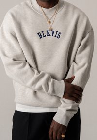 Sudadera gris de cuello redondo con el bordado "BLKVIS" en azul marino, puños y dobladillo acanalados, que presenta una textura suave y un corte relajado.