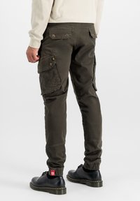 Pantaloni cargo din twill verde măsliniu, cu buzunare laterale, manșete elasticizate, buzunare spate cu nasturi și pantofi negri cu tălpi verzi.