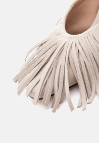 Chaussure en daim beige avec plusieurs longues bandes fines de franges couvrant la zone des orteils.