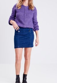 Fialový pletený svetr s knoflíky a ohrnutými rukávy, doplněný modrou džínovou minisukní s předními kapsami a patentními detaily.