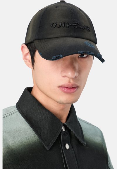Cappellino da baseball nero con bordi consumati, caratterizzato da testo ricamato sul davanti. Indossato con una maglietta bicolore, che presenta un colletto scuro.