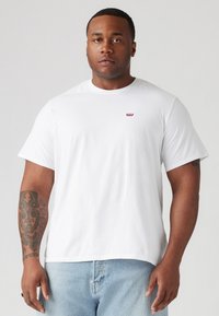 Witte katoenen t-shirt met korte mouwen, ronde hals en een klein rood Levi's logo op de borst. Gecombineerd met lichtblauwe denim jeans.