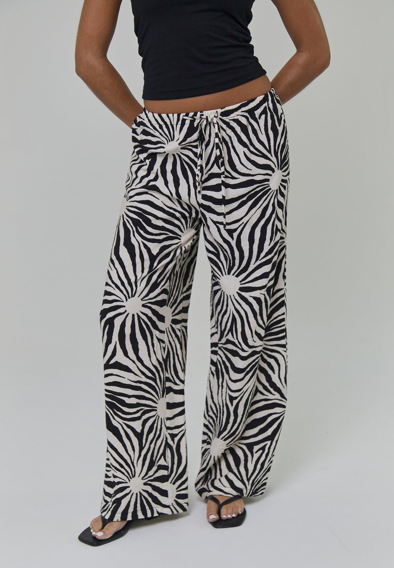 Pantaloni a gamba larga a righe bianche e nere con un motivo a raggi di sole, con una vita con coulisse e un tessuto morbido e strutturato.