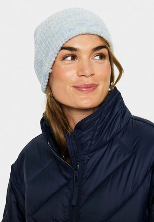 Hellblauer Strickbeanie mit gerippter Textur, aus weichem Material gefertigt. Getragen mit einer dunkelblauen isolierten Jacke mit Zip-Verschluss.