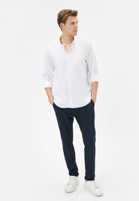 Witte langarmshirt met eenbutton-down kraag en borstzak, gecombineerd met marineblauwe broek en witte sneakers. Soepele katoenstof.