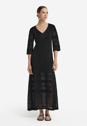 Schwarzes gestricktes Maxikleid mit V-Ausschnitt und dreiviertellangen Spitzenärmeln, das vertikale Rippungen, filigrane Muster und eine lockere Passform aufweist.