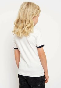 White cotton t-shirt with short sleeves, featuring navy blue ribbed cuffs. The shirt has a straight cut and is paired with dark denim shorts.
