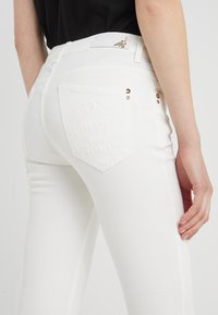 Vita denimjeans med en figurnära design, som har bakfickor med präglade detaljer och metalliska accenter på midjan.