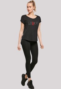 Juodas sportinis marškinėliai su baltu ir raudonu „LOVER“ grafiką, derinami su juodais leggingais ir sportinėmis bateliais, su trumpomis rankovėmis ir laisvu kirpimu.