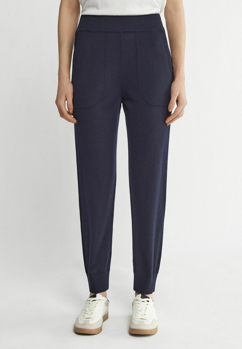 Marine jogger broek met een zachte textuur, elastische tailleband, voorzakken en taps toelopende boorden. Gecombineerd met witte sneakers voor contrast.