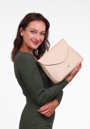 Beige vegan leather handbag with a structured design, flap closure, silver logo detail, held against a white background.