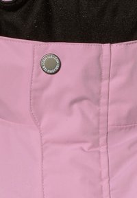 Rosa vattentätt tyg med synlig sömnad; har en rund silverknapp präglad med varumärkesnamn. Svart översida ovanför den rosa delen.