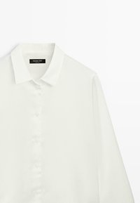 Witte blouse met lange mouwen en knopen, voorzien van een puntige kraag, afgebeeld tegen een effen witte achtergrond.