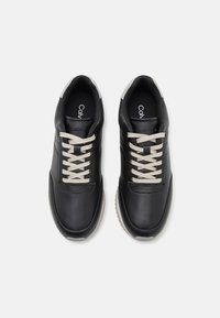 Černé kožené tenisky se světle šedými tkaničkami, zaoblený tvar, texturovaný svršek a značka Calvin Klein na stélkách.