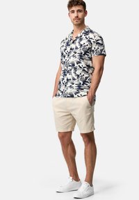 Camisa de manga corta, abotonada, en color marino con un patrón tropical blanco, combinada con pantalones cortos beige y zapatillas blancas.