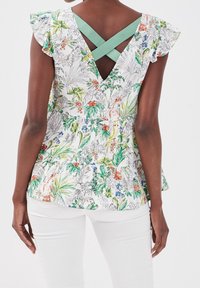 Floral peplum blouse in white fabric featuring green, orange, and blue patterns, with ruffled sleeves and a V-back design with crisscross straps.