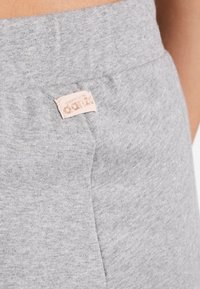 Szare bawełniane spodnie dresowe mają szeroką elastyczną talię, boczne kieszenie oraz małą, jasnoróżową metkę marki wszytą na pasku w talii.