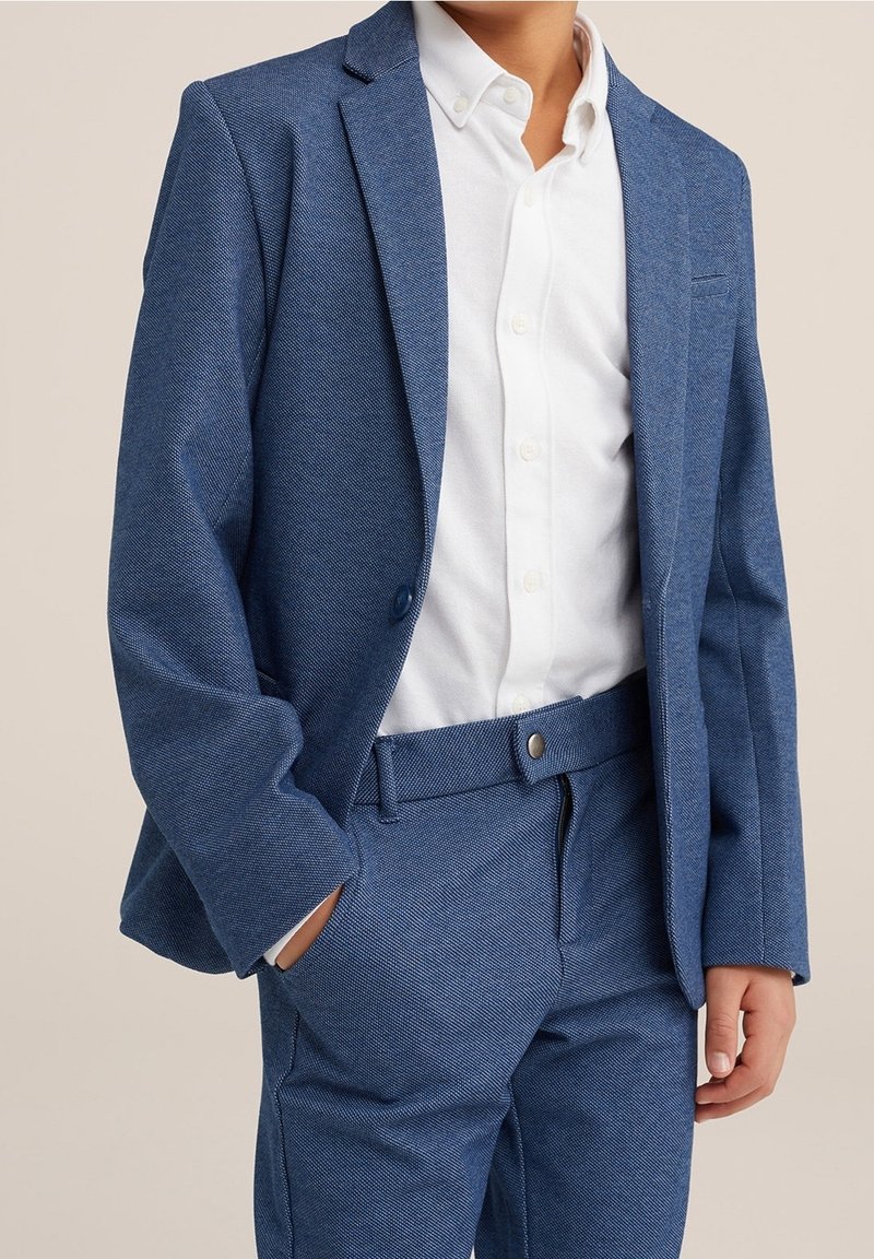 Giacca da completo intrecciata blu con rever a taglio, abbinata a una camicia bianca con bottoni, caratterizzata da una vestibilità su misura e un tessuto testurizzato.