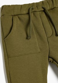 Pantalones deportivos de color verde oliva hechos de tela de algodón texturizada, con cinturilla elástica, cierre con cordón y bolsillos delanteros.