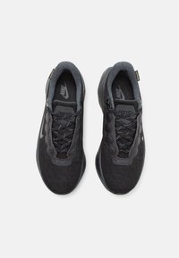 Baskets Nike noires avec un dessus en mesh texturé, lacets noirs plats et une semelle lisse. Présente des accents réfléchissants subtils et un logo sur la languette.
