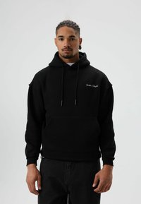 Zwarte hoodie met buidelzak, verstelbare capuchon en geborduurd logo op de borst. Gemaakt van zacht materiaal, met een relaxte pasvorm en geribbelde manchetten.
