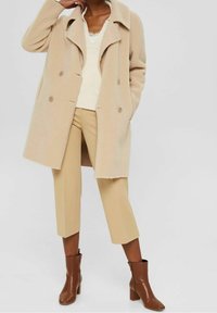 Manteau beige croisé en polaire, stylé avec un pull crème et un pantalon beige taille haute, complété par des bottines marron.