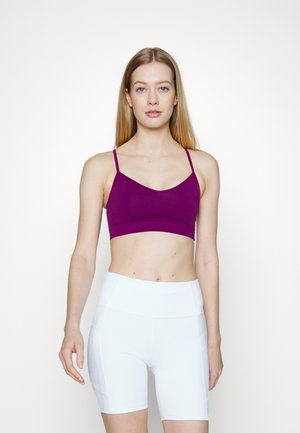 Sutiã desportivo roxo com alças finas, apresentando uma textura suave e um design minimalista. Combinado com calções atléticos brancos de cintura alta.